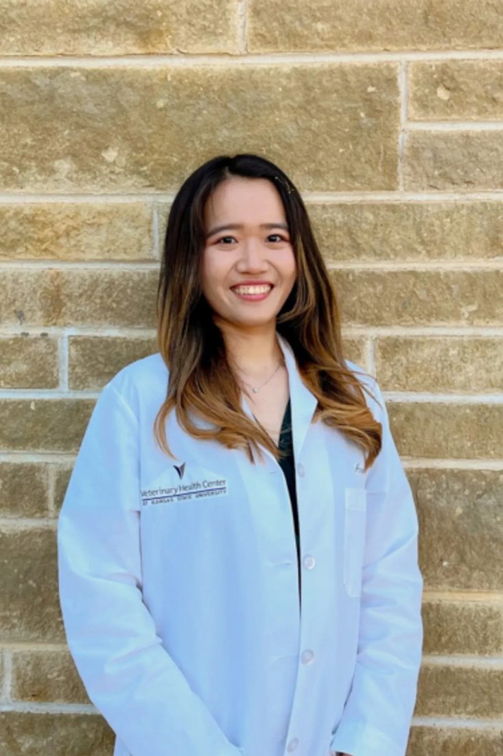 Smiling female veterinarian in white coat standing against a stone wall