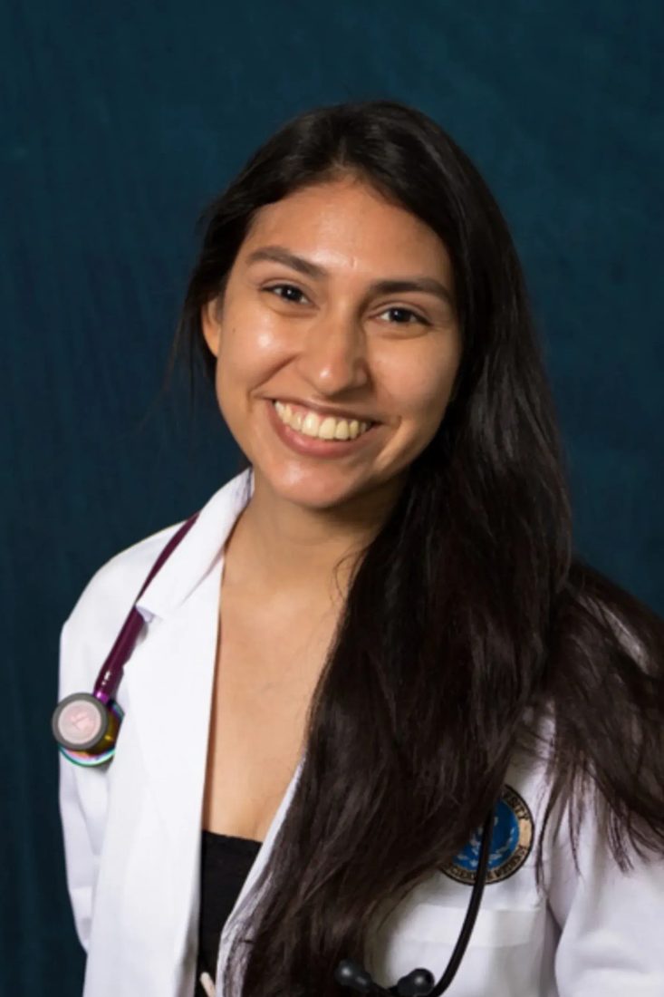 Smiling female veterinarian with stethoscope in white coat against dark blue background